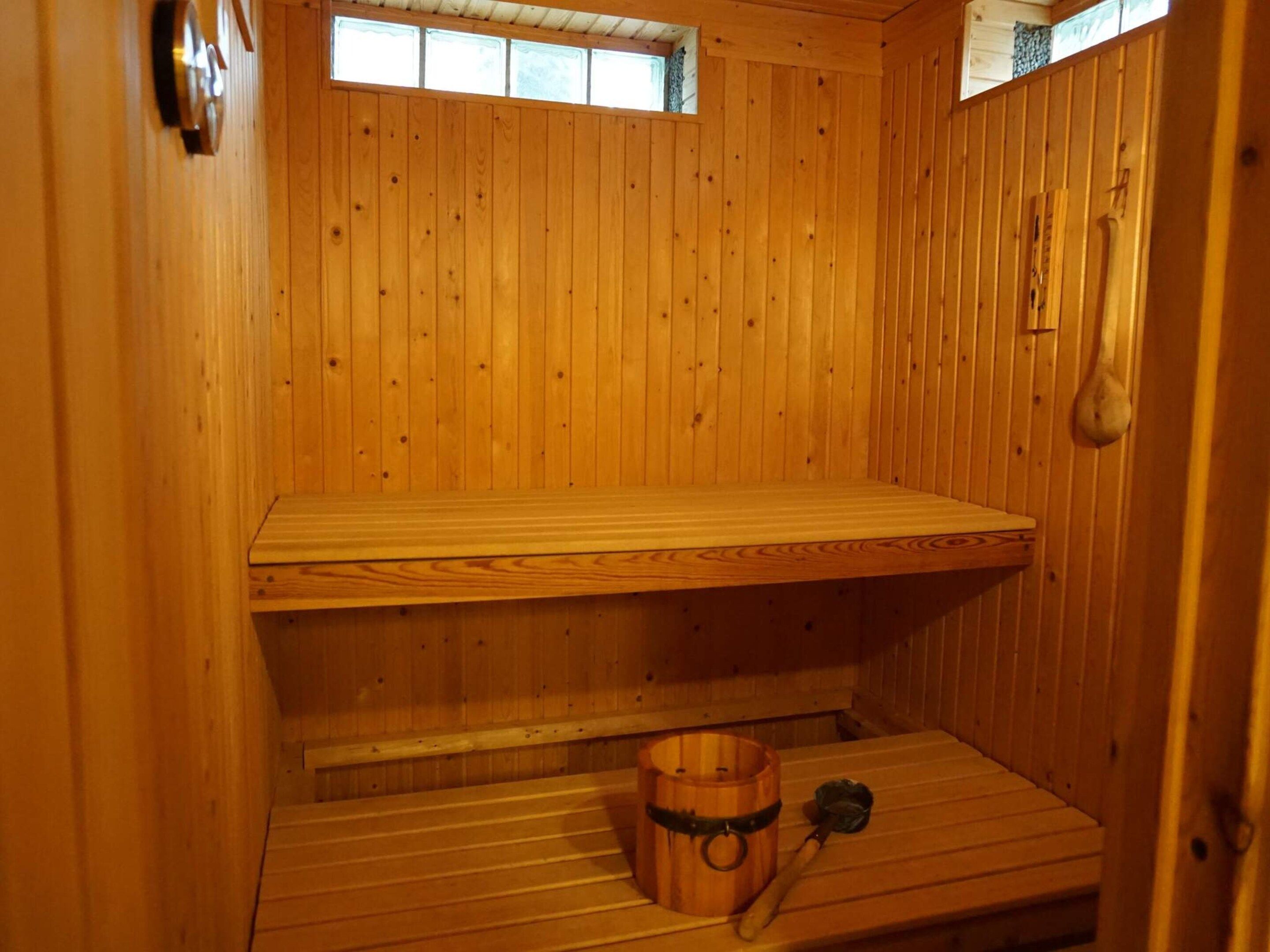 Eine Sauna mit Holzwänden, einer Sitzbank, einem Eimer und einer Bürste.
