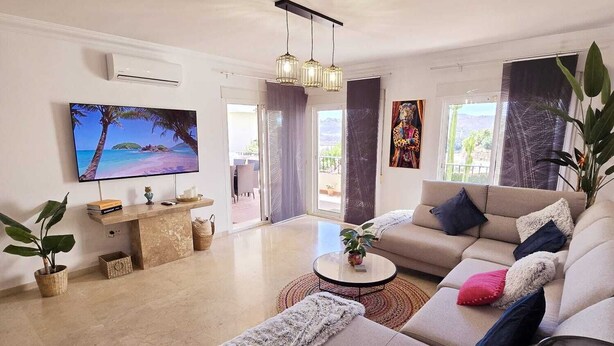 Un soggiorno moderno con un divano color beige, un tavolino da caffè e una TV a parete.
