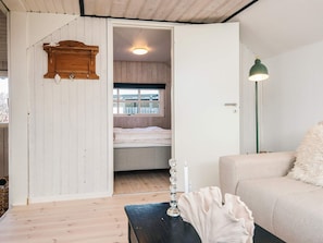 Quarto com cama, cabeceira de madeira, parede branca, luminária de chão e um banquinho.