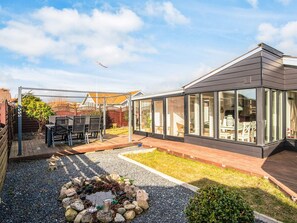 Ein modernes Haus mit Wintergarten, einer Terrasse mit Gartenmöbeln und einem dekorativen Felsenbeet.