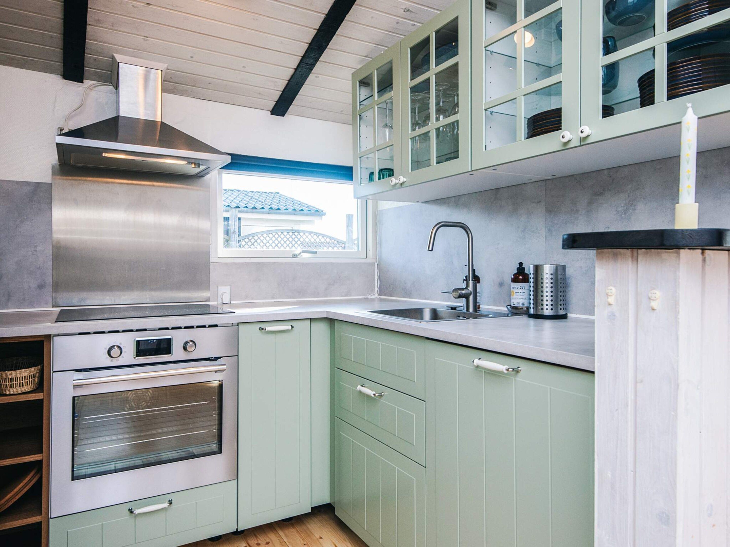 A kitchen with a stainless steel range hood, a built-in oven, a sink with a modern faucet, and light green cabinets.