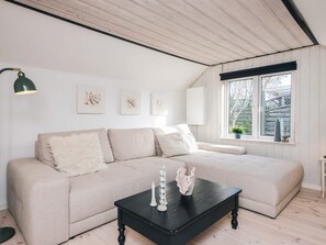 A modern living room with a beige sofa, a black coffee table, and a window with a view of a wooden fence.