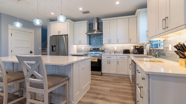 Una cocina moderna con armarios blancos, un refrigerador de acero inoxidable, horno empotrado y una isla grande con taburetes de bar.