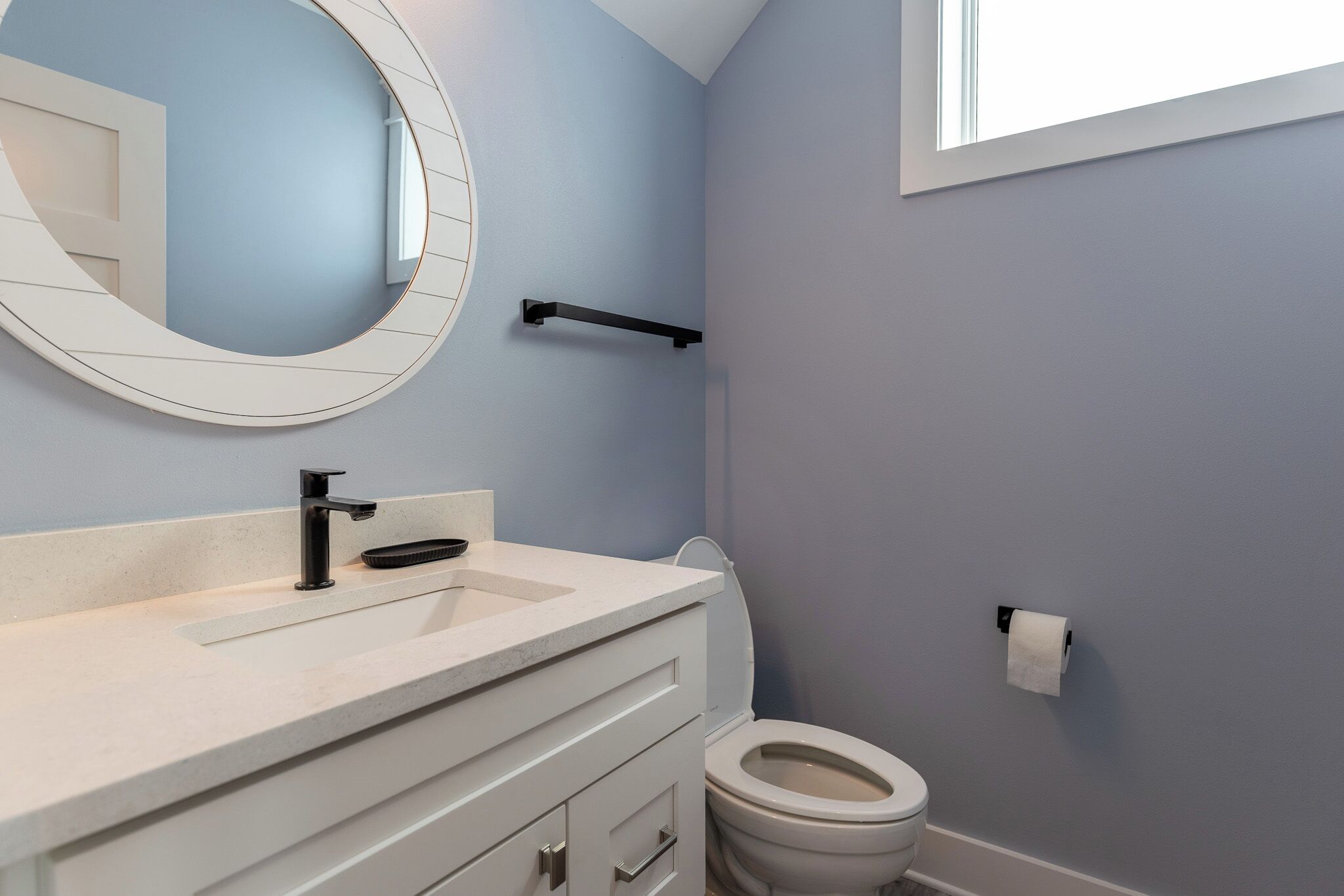 A bathroom with a white vanity, a round mirror, a black towel rack, and a toilet.