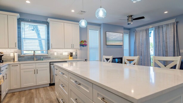 Une cuisine moderne avec des meubles blancs, un grand îlot central et des luminaires suspendus.