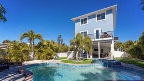 Una casa de dos pisos con piscina, rodeada de palmeras y un césped cuidado.