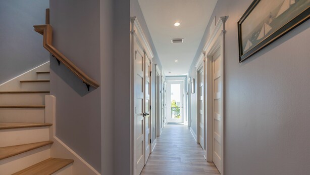 A hallway with a wooden staircase, white doors, and a framed picture on the wall. - Dolphins Delight: Rooftop deck, large heated pool, hot tub (Anna Maria)