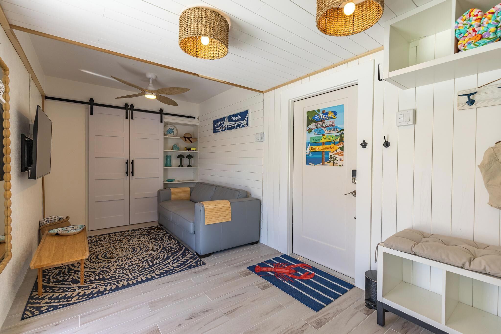 A compact living space with a sofa, a small table, a ceiling fan, and a door with a colorful poster.