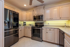 Una cocina moderna con electrodomésticos de acero inoxidable, armarios de colores claros y piso de baldosas.