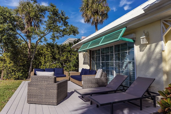 Una terrazza esterna con mobili in vimini, tra cui divani e poltrone relax, e una porta vetrata che dà su una zona coperta.