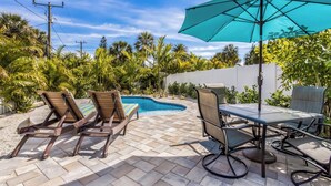 Une terrasse avec une piscine, des chaises longues et une table avec un parasol.