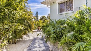Un chemin menant à une maison entourée d’une végétation luxuriante et de palmiers.