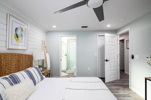 Ein Schlafzimmer mit Bett, Deckenventilator, gerahmtem Kunstwerk und einem Holzkopfteil.
