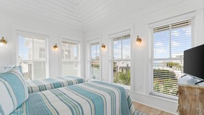 Ein Schlafzimmer mit zwei Betten, weißen Wänden und großen Fenstern mit Jalousien.