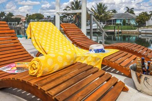 A poolside lounge area with wooden loungers, a yellow patterned towel, and a bucket of beer bottles. - Waterfront Home | Pool, Hot Tub, Kayak, & Billiards (Marco Island)
