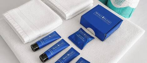 A set of toiletries including a shampoo bottle, hand wash, and soap, arranged on a white towel with a blue box and two towels.
