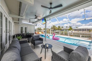 A spacious outdoor area with a pool, lounge chairs, and a television screen. - Waterfront Home | Pool, Hot Tub, Kayak, & Billiards (Marco Island)