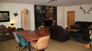 A living room with a wooden dining table, two sofas, a coffee table, and a large painting on the wall. - Altstrimmig Shine (Altstrimmig)
