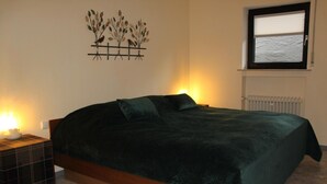 A bedroom with a bed, a nightstand, a wall art piece, a window, and a radiator. - Altstrimmig Shine (Altstrimmig)