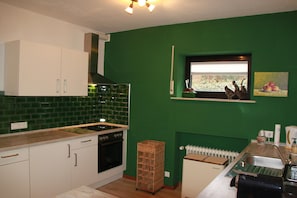 Una cocina con paredes verdes, armarios blancos, un ventanal con vistas y un lavamanos.