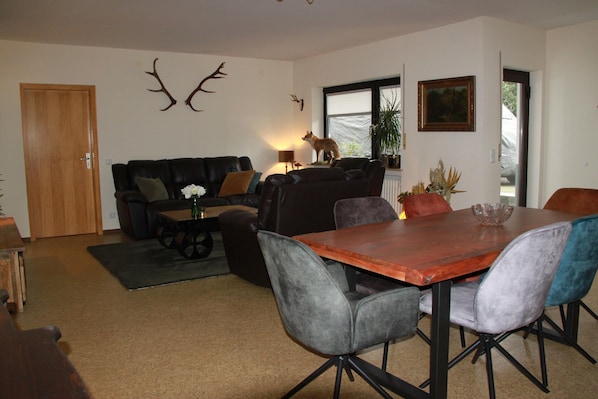 Una sala de estar con una mesa de comedor de madera, sillas tapizadas de gris, un sofá de cuero negro y una puerta de madera.