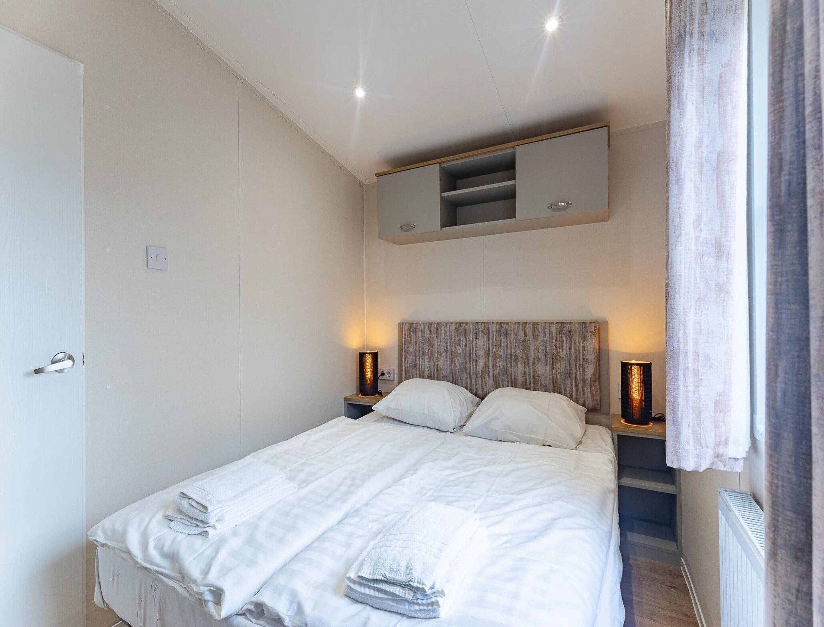 A bedroom with a bed, bedside lamps, a built-in shelf above the bed, and a door.