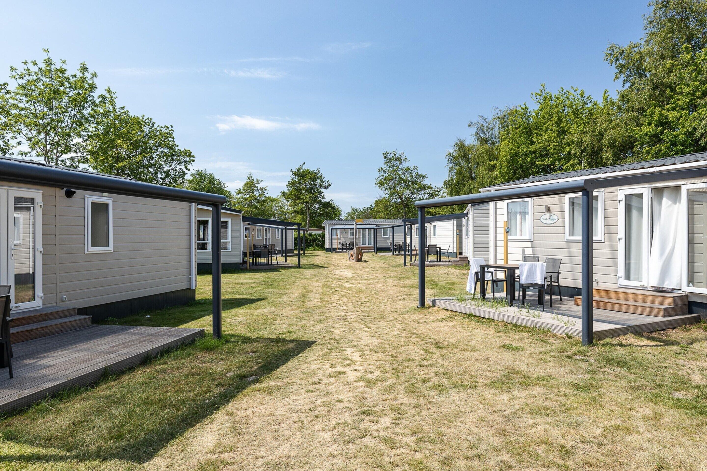 A row of mobile homes with outdoor seating areas, each with a small deck and a table.