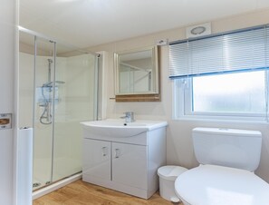 A bathroom with a glass-enclosed shower, a white sink, a toilet, and a window with blinds. - 2-bedroom Family Retreat Near Dunes (Burgh-Haamstede)