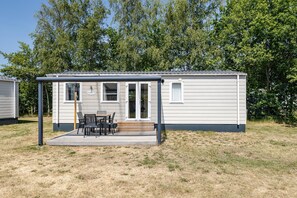 A single-story mobile home with a covered patio area, a small deck, and a windowed entrance. - 2-bedroom Family Retreat Near Dunes (Burgh-Haamstede)