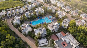 An aerial view of a residential area with multiple houses, a central swimming pool, and surrounding greenery. - Cozy 2-bedroom apartment in charming Beach with AC and gym access (Beach)