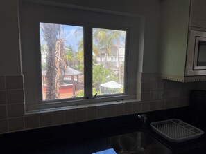 A kitchen with a window overlooking a garden, a sink, and a microwave. - Cozy 2-bedroom apartment in charming Beach with AC and gym access (Beach)