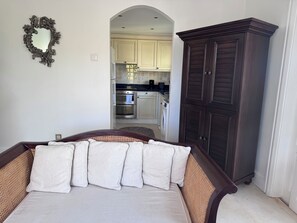 A bedroom with a bed, a dark wooden wardrobe, and a kitchen visible through an archway. - Cozy 2-bedroom apartment in charming Beach with AC and gym access (Beach)