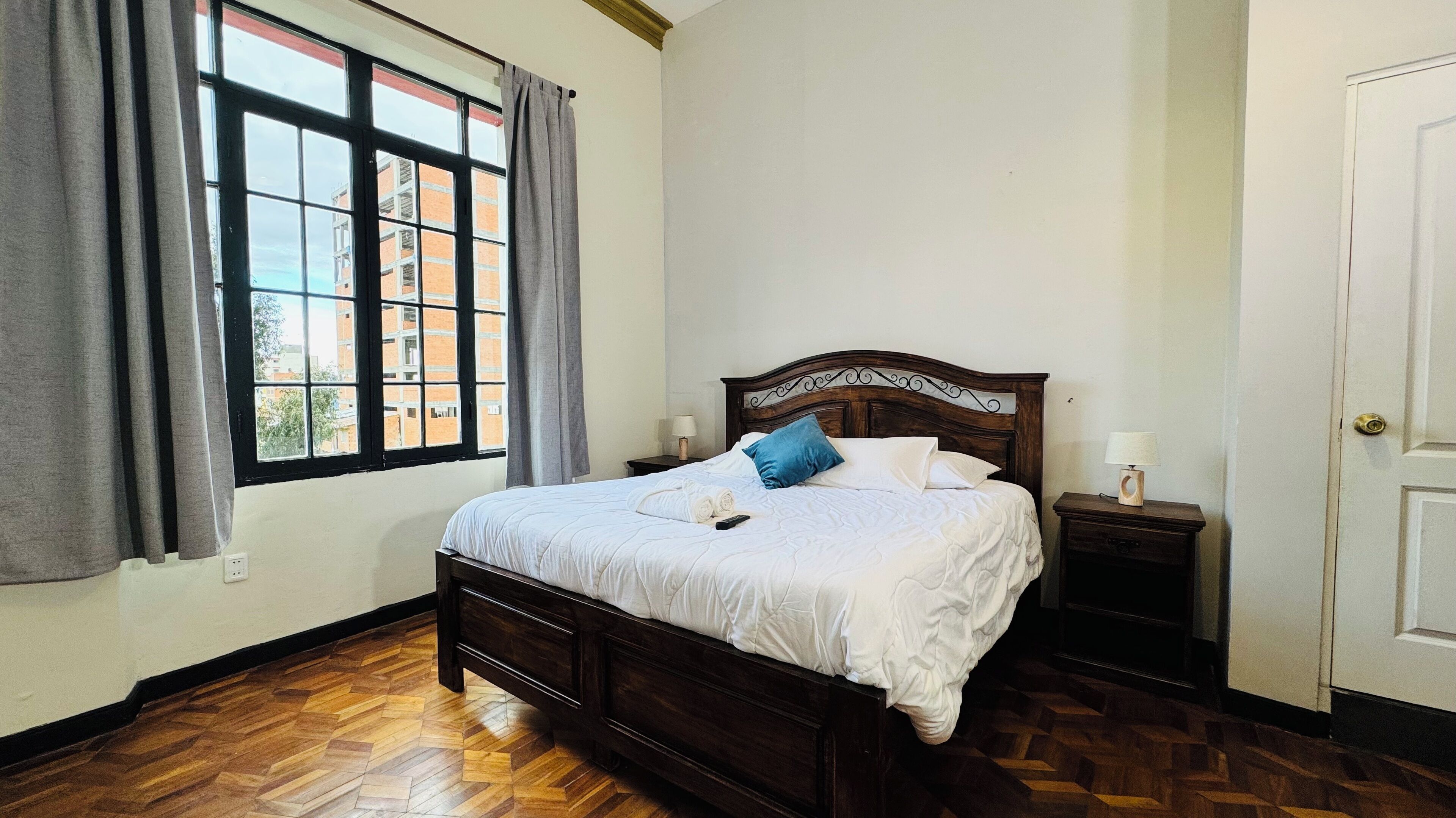 A bedroom with a wooden bed, a nightstand, a window with curtains, and a door.