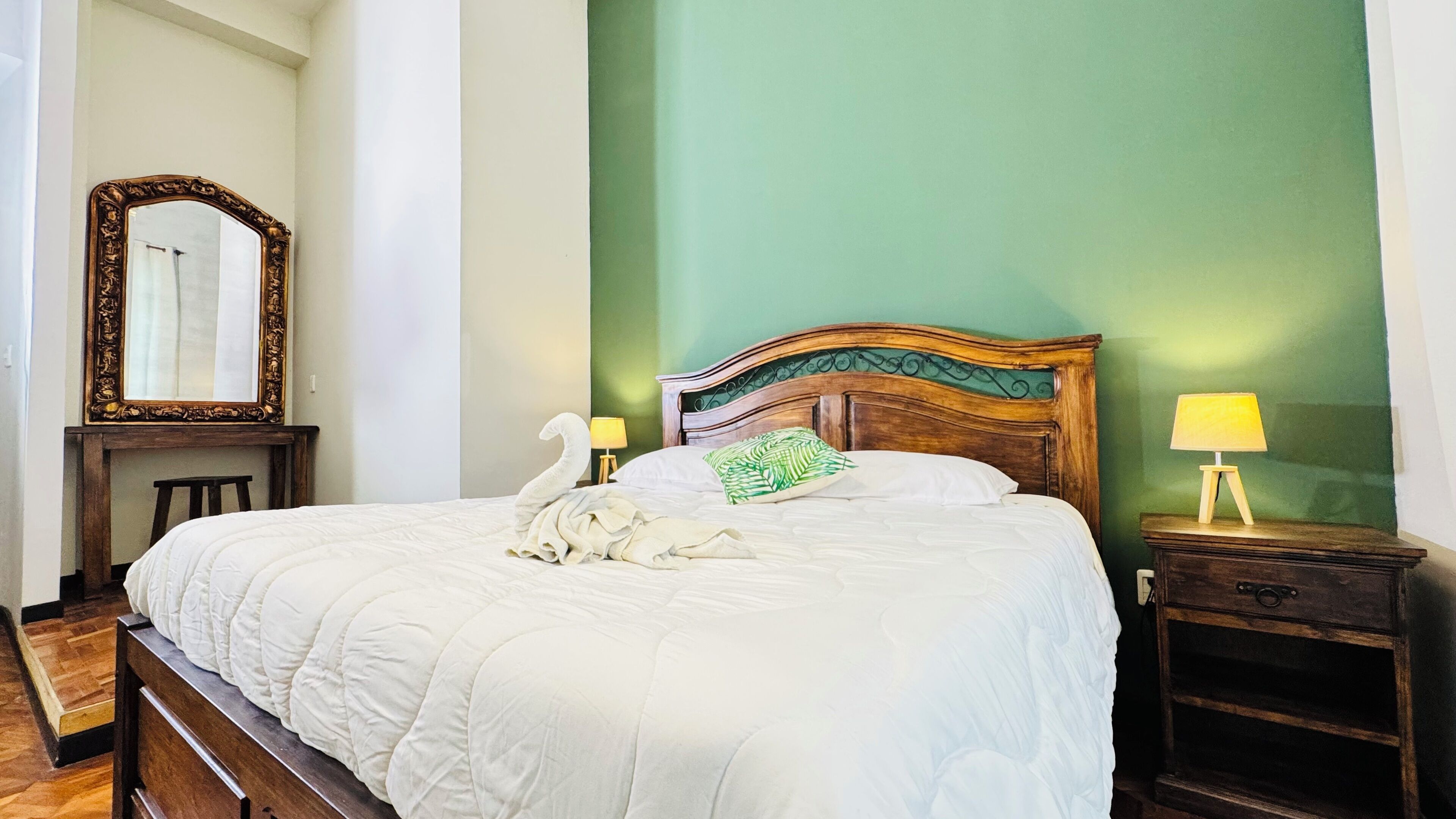A neatly made bed with a wooden headboard, a bedside table with a lamp, and a mirror on the wall.