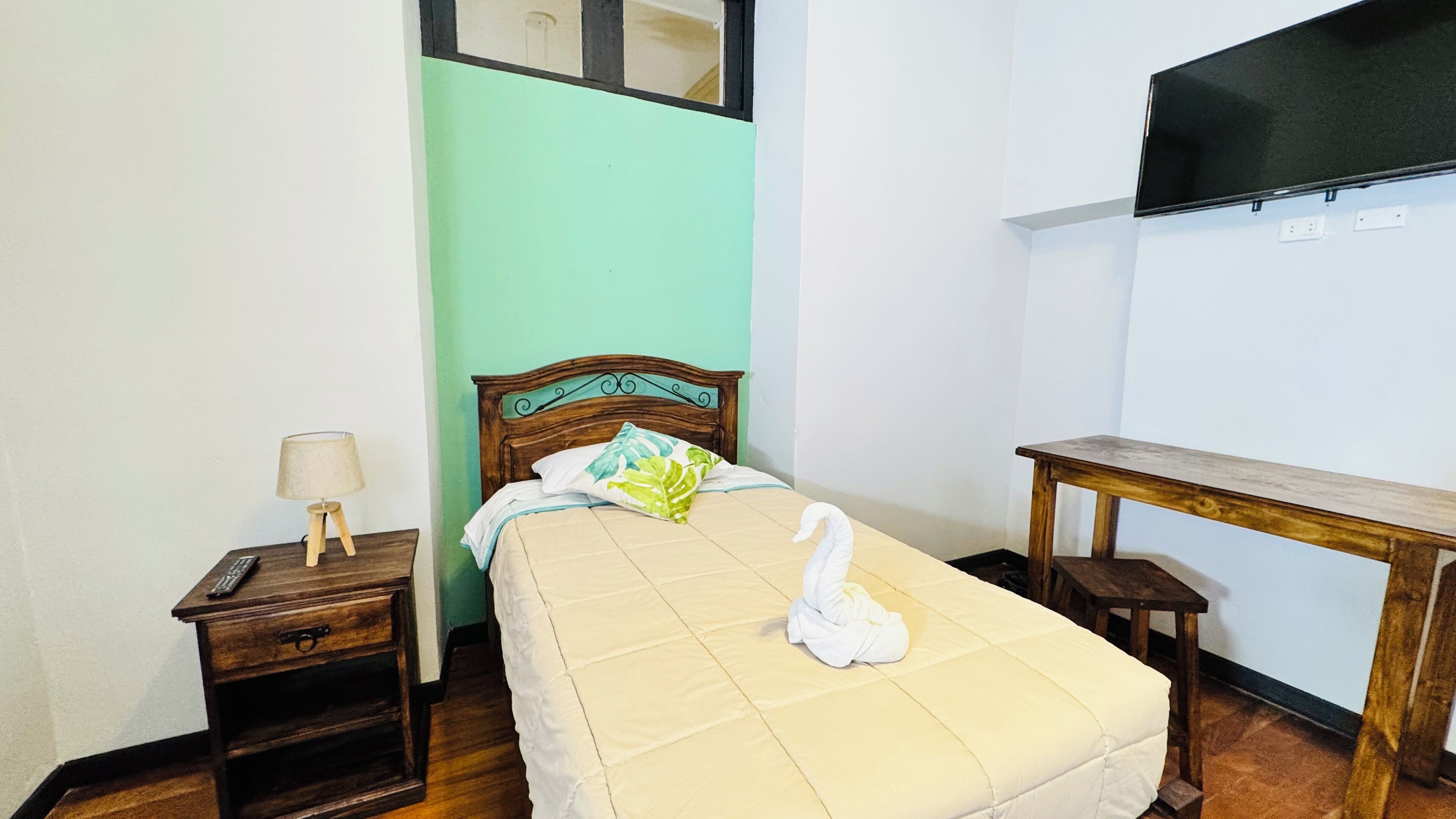 A neatly made bed with a white towel, a wooden nightstand with a lamp, and a small wooden table.
