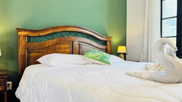 A bed with a wooden headboard, a green pillow, and a swan-shaped towel.