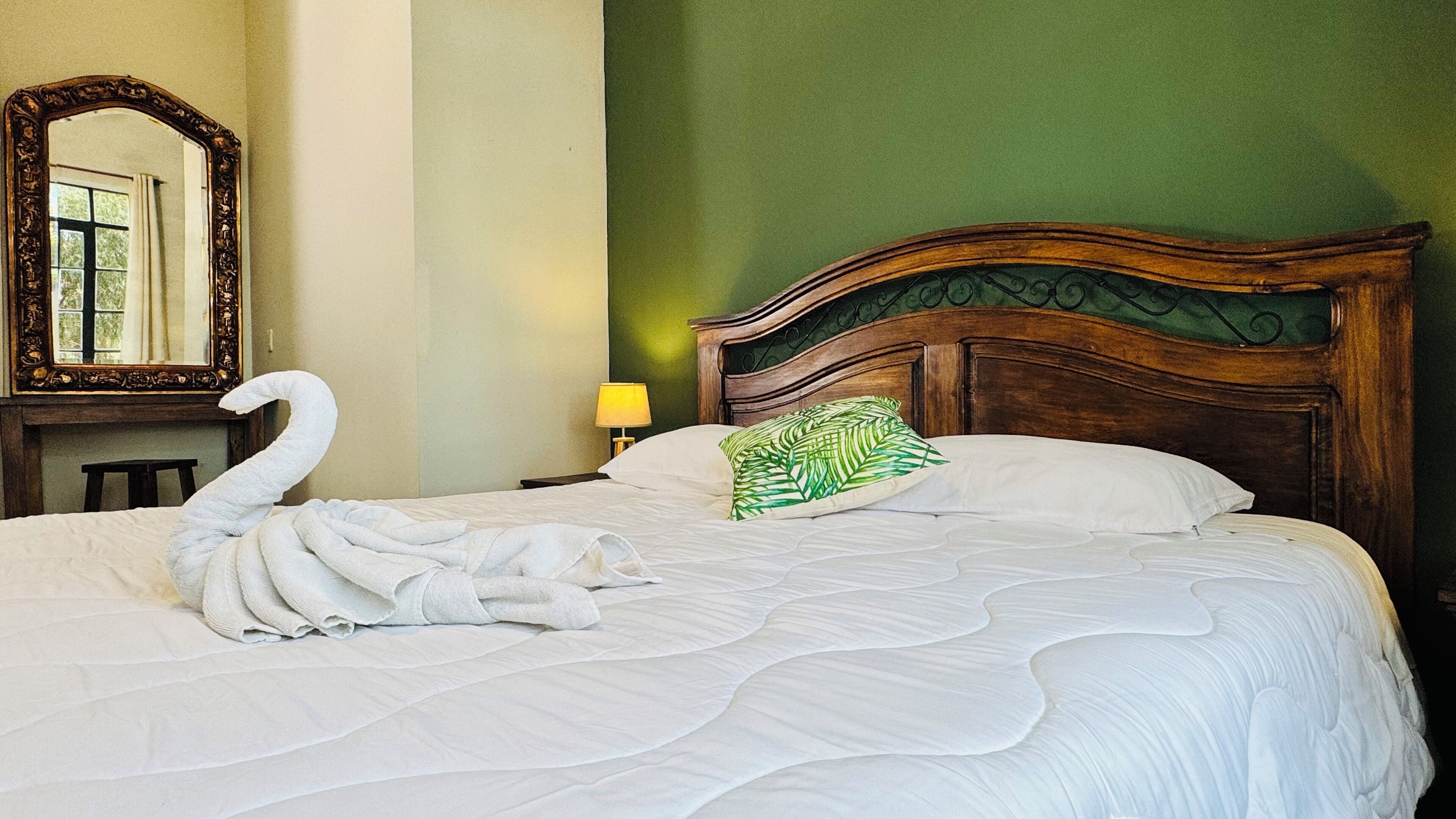 Una cama con una toalla con forma de cisne, una almohada verde y un cabecero de madera.