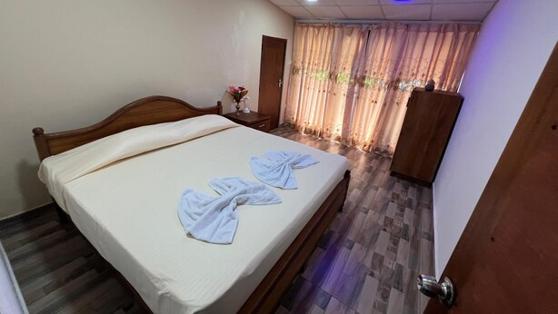 A hotel room with a wooden bed, a nightstand with a vase of flowers, a wardrobe, and a window with curtains.