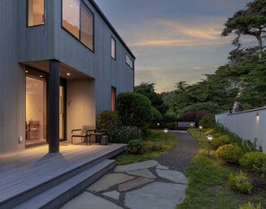 A modern house with a wooden deck, a stone pathway, and a well-maintained garden. - Hedgerow Haven | Premium Oceanfront with Hot Tub (The Sea Ranch)