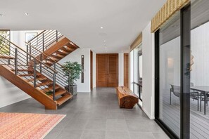 A modern interior with a wooden staircase, a bench, and a glass door leading to an outdoor area. - Hedgerow Haven | Premium Oceanfront with Hot Tub (The Sea Ranch)