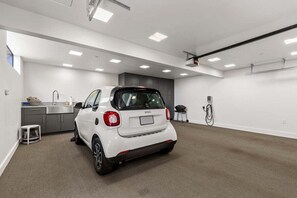 A white car parked in a modern, well-lit garage with a kitchen area in the background. - Hedgerow Haven | Premium Oceanfront with Hot Tub (The Sea Ranch)