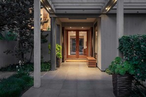A modern building entrance with a concrete facade, a wooden door, and a small set of steps leading to the entrance. - Hedgerow Haven | Premium Oceanfront with Hot Tub (The Sea Ranch)