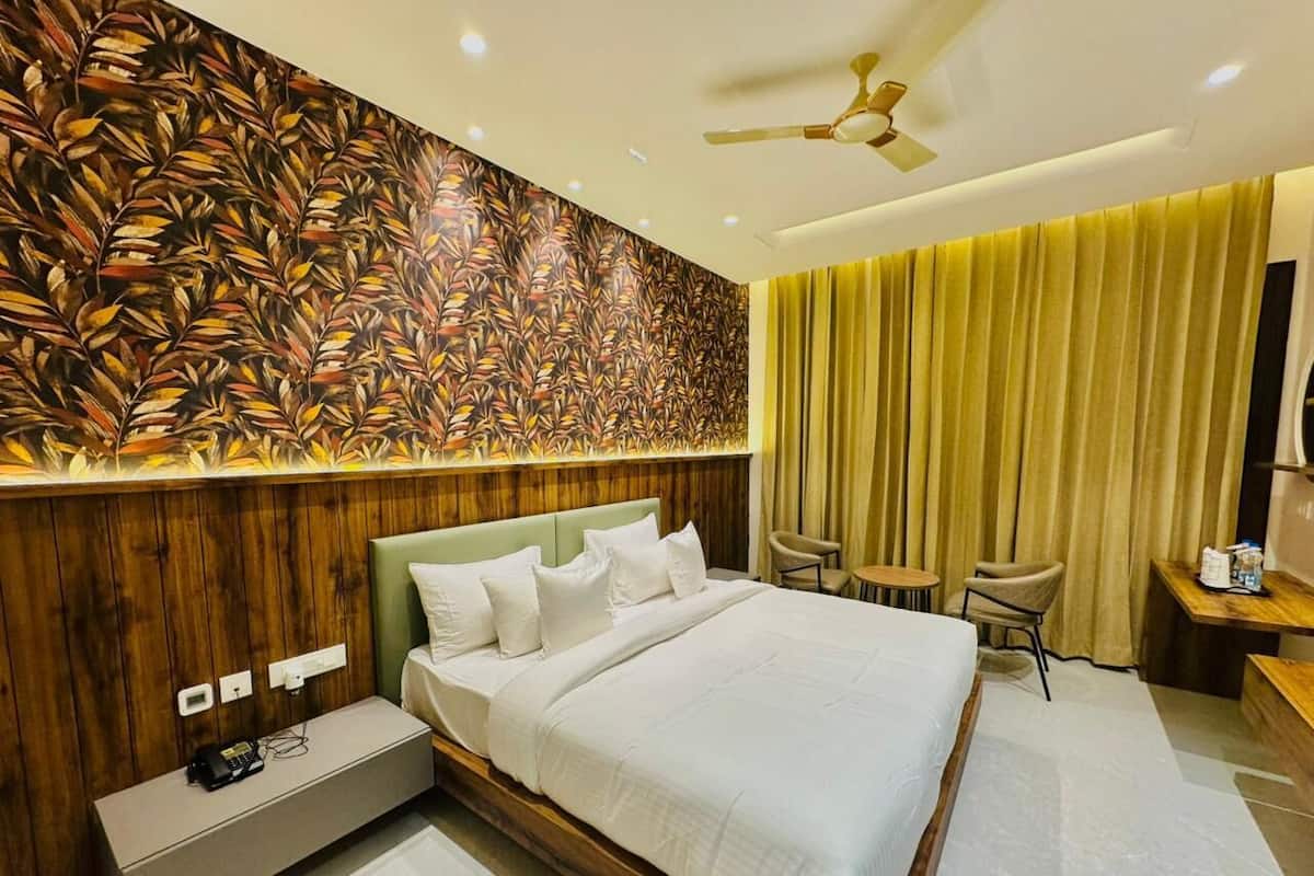 Una habitación de hotel con una cama grande, un cabecero de madera, una pared con diseño de hojas, un ventilador de techo, un escritorio con silla y una ventana con cortinas.