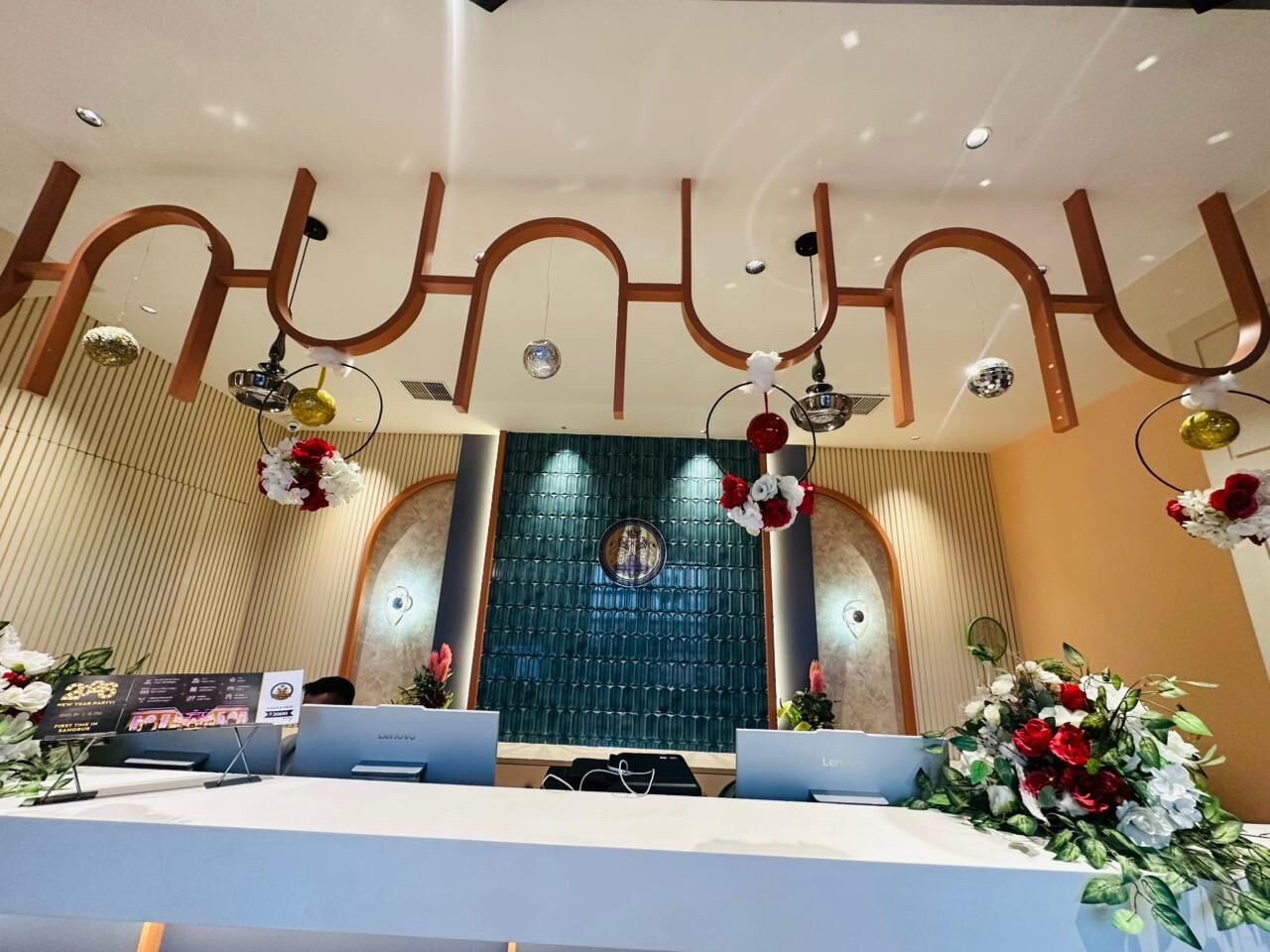 Zona de recepción con diseño moderno, que incluye un mostrador de recepción, dos computadoras portátiles y arreglos florales decorativos.
