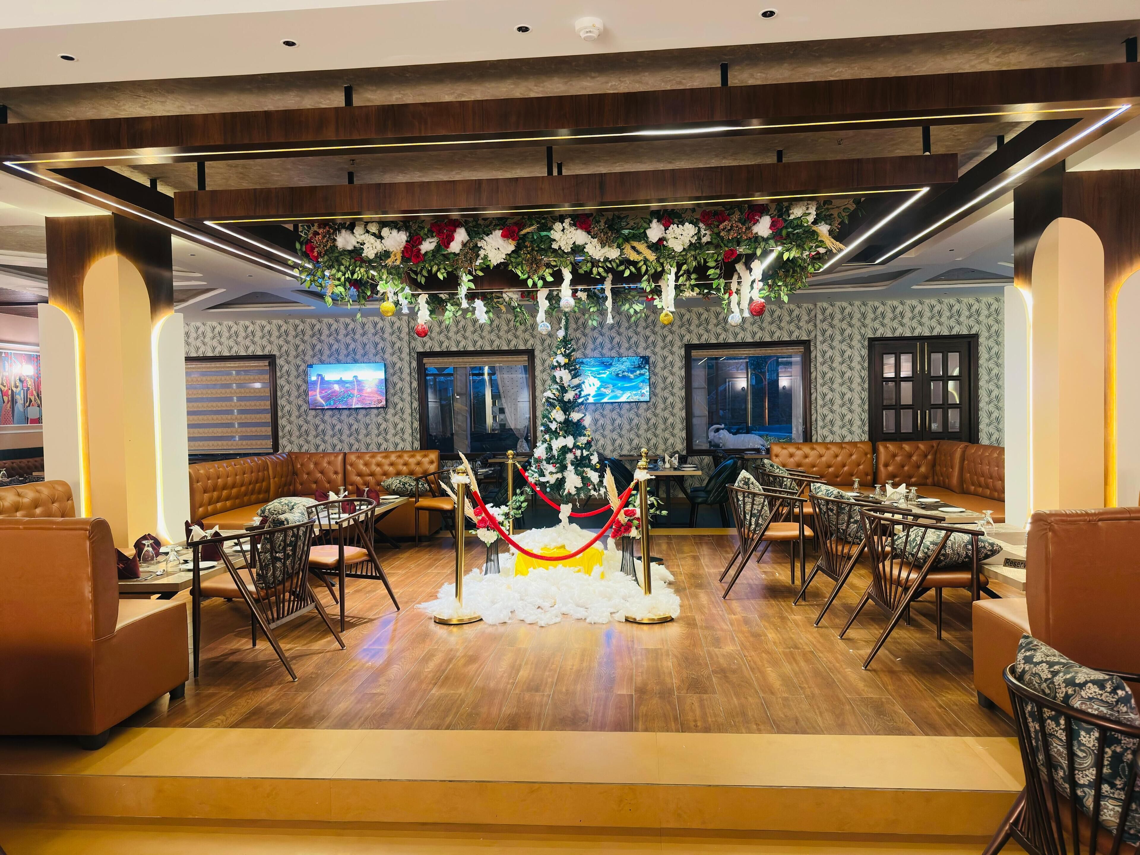 A modern hotel lobby with a central floral arrangement, seating areas, and a television screen.