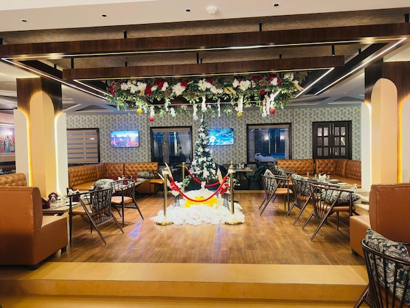 Un hall d'hôtel moderne agrémenté d'une composition florale centrale, de coins salon et d'un écran de télévision.
