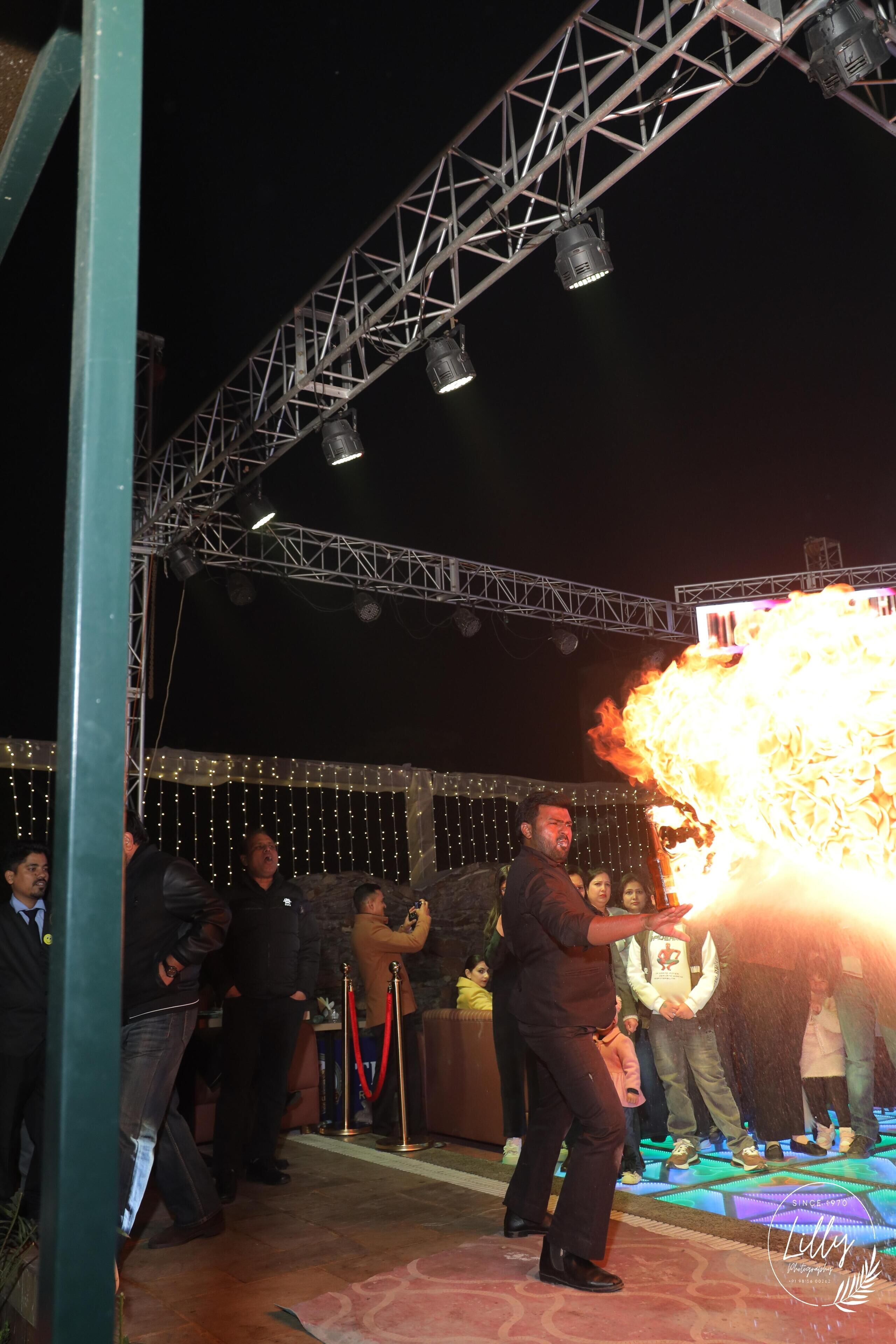 A stage with a performer in black, a crowd, and a large fire effect.