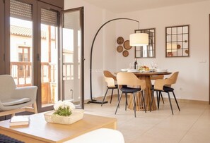 A dining area with a table set for four, surrounded by chairs, a floor lamp, and a wall-mounted mirror. - Sunny Apartment for 4 in Vera (Arona)