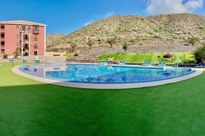 A swimming pool with blue water, surrounded by green artificial grass, and a red building in the background. - Sunny Apartment for 4 in Vera (Arona)