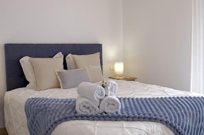 A neatly made bed with rolled towels, a blue blanket, and a bedside lamp. - Sunny Apartment for 4 in Vera (Arona)